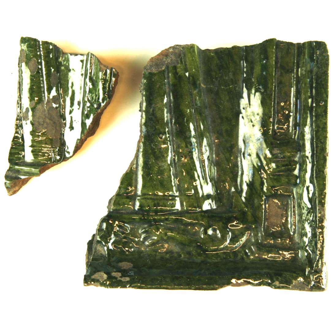 2 fragmenter af grønglasserede kakler. Fra samme form. Nederste højre hjørne. I midten nederdel af kvindekjole. Indrammet af søjle. Rammestykke forneden rummer en slange og foreste del af et andet dyr. Høj yderkant. Største mål: 14 cm.