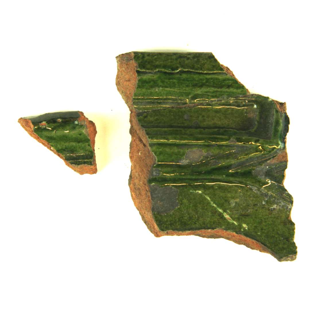 Tre fragmenter, heraf to sammenlimede af grønglasserede kakler. Det største stammer fra øverste venstre hjørne, og viser rester af søjle, svarende til foregående. Det andet har kun yderkant og begyndelse til søjlen. Største mål: 3,5 og 7,2 cm.