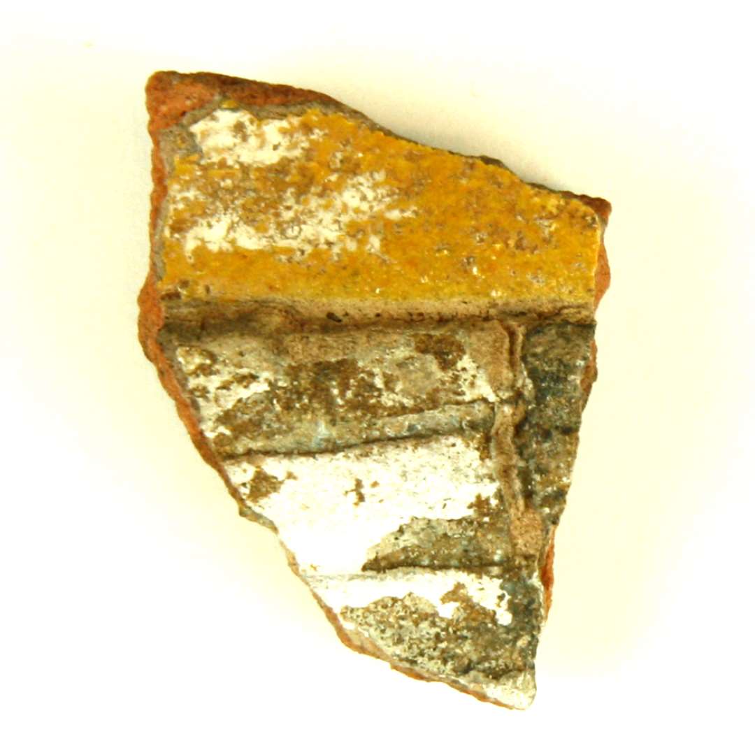 Fragment af polykrom, lodret kakkel. 1 stykke. Del af motiv med dame i renæssancedragt. Del af underkjolen. Største mål: 4,7 cm.