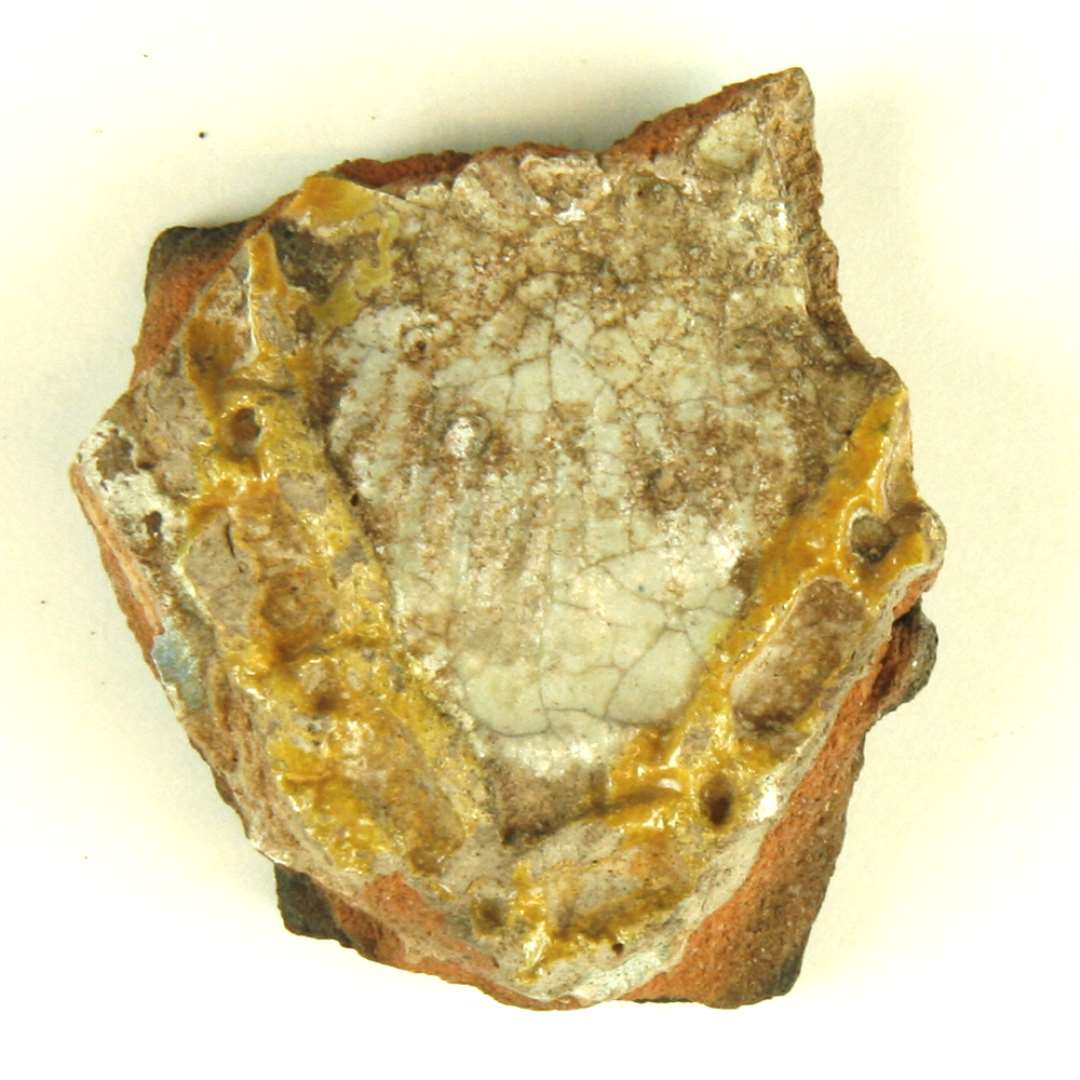 Fragment af kpolykrom, lodret kakkel. Del af motiv med dame i renæssancedragt: Brystparti med gylden kæde. Største mål: 4,5 cm.