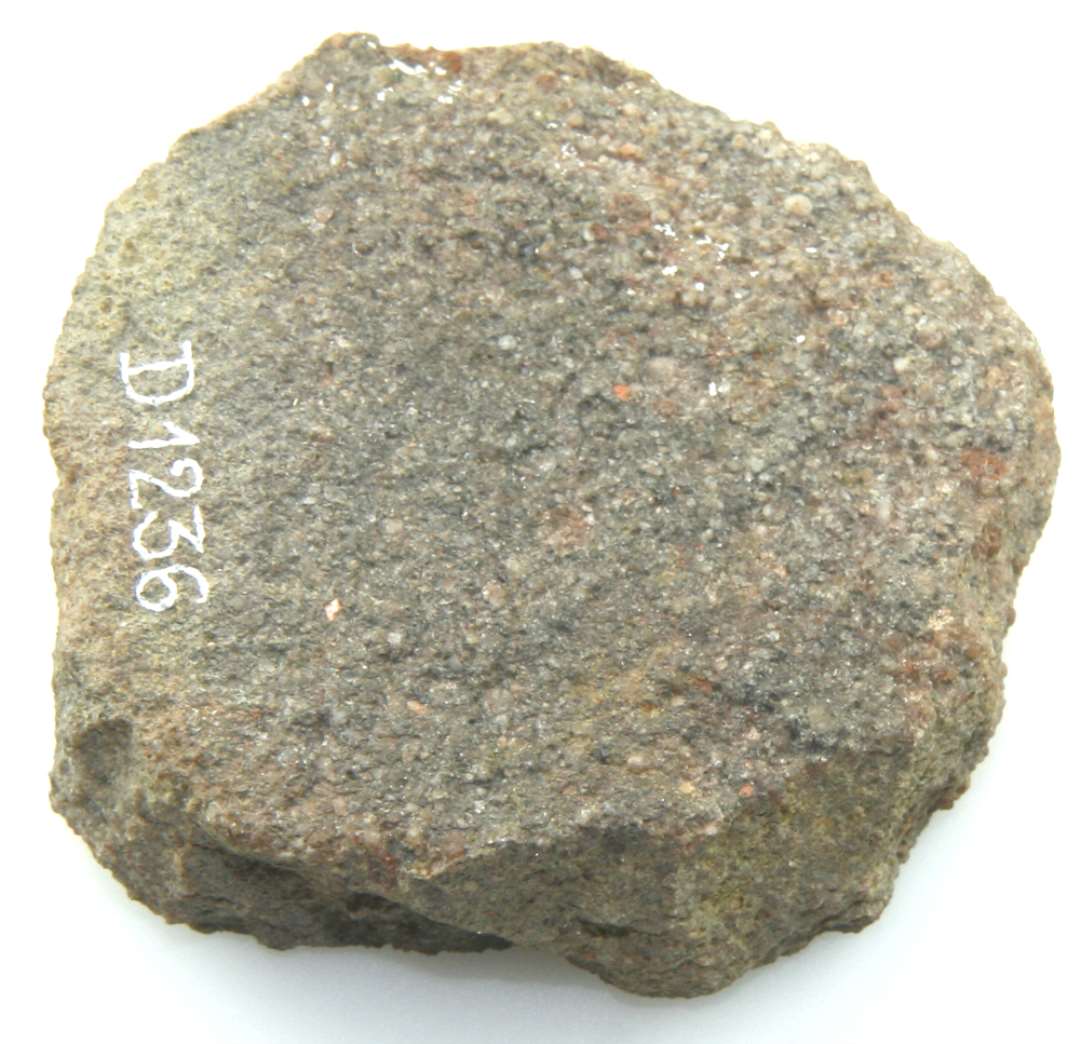 Stenskive af bjergart af uregelmæssig cirkulær form, med plan over og underside og groft afhuggede kanter. Diameter: ca. 6 cm. Tykkelse: ca. 2 cm.