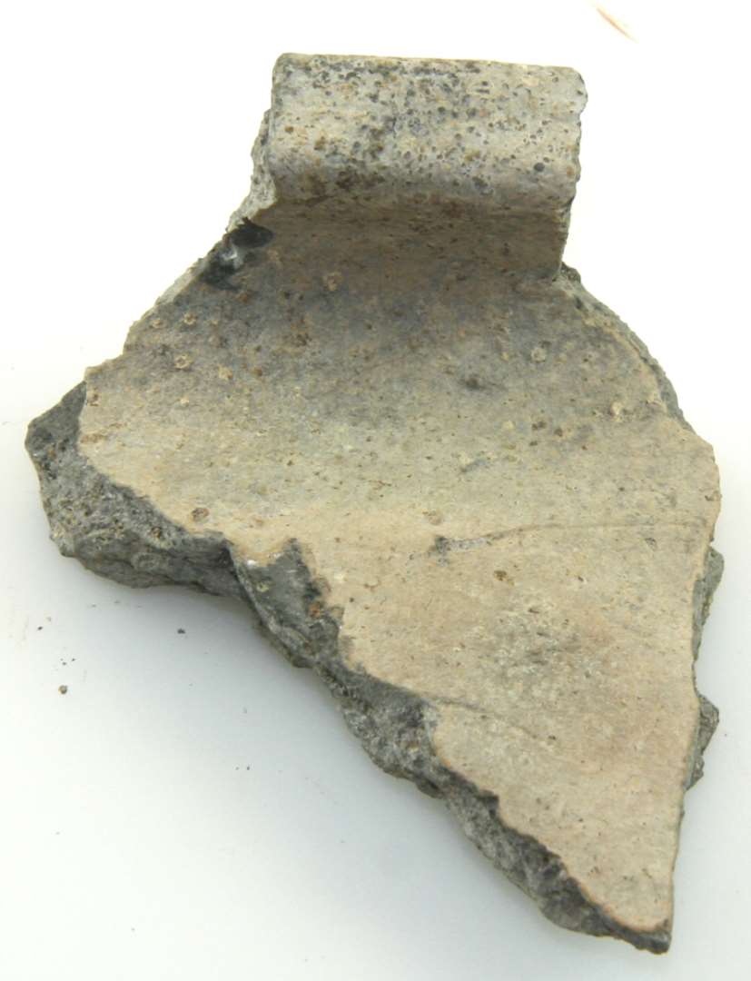 Randskår af gråbrændt uglaseret lertøj med brunlig overflade. Groft gods. Største højde: 6,8 cm. Bredde: 5,2 cm. Skærv:  0, 5 cm.