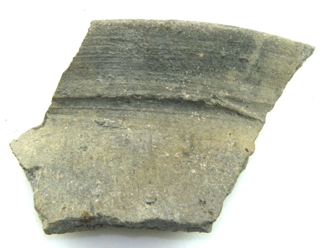 Randskår af gråbrændt uglaseret lertøj med grå overflade. Største højde: 4,8 cm. Bredde: 5,2 cm. Skærv: 0, 7 cm.