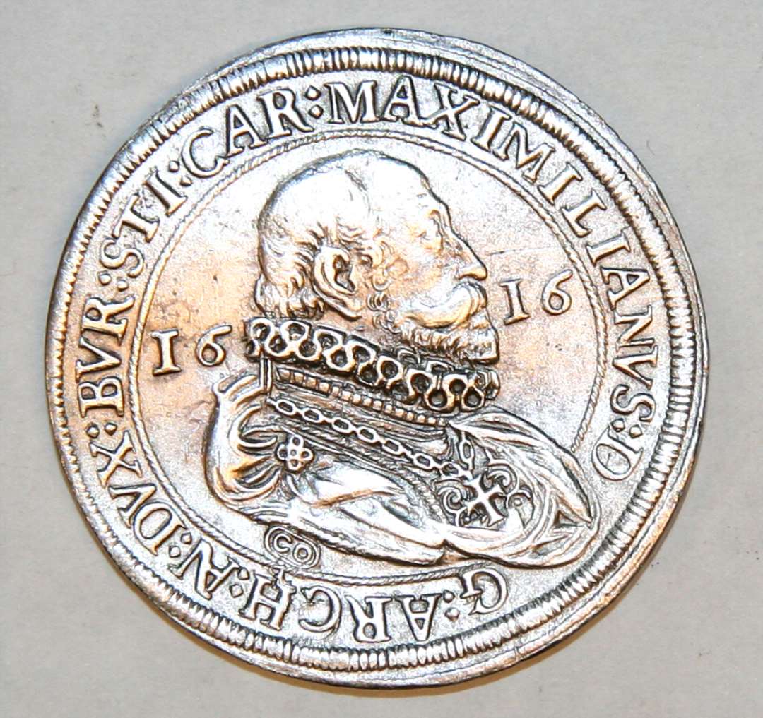 Mønt af sølv, 4,2 cm. i diameter. Mønten er slået for ærkehertug Maximilian af Tyrol (1612-18) af møntmester i Hall: Cristoph Orber, hvis mærke ses under ærkehertugens buste. Forsidens omskrift er i sin fulde længde: MAXIMILIANUS : DEI GRATIA : ARCHIDUX : AUSTRIAE : DUX : BURGUNDIAE : STIRIAE :CARINTHIAE : (bagsiden) ET : CARNIOLAE : MAGISTERII : PRUSSIAE : ADMINISTRATOR : COMES : HABSBURGENSIS : ET : TIROLIS. Dalere fra Maximilian af Tyrol med forskellige årstal er i det hele taget ikke  ualmindelige i danske fund.   NM: FP 2830.