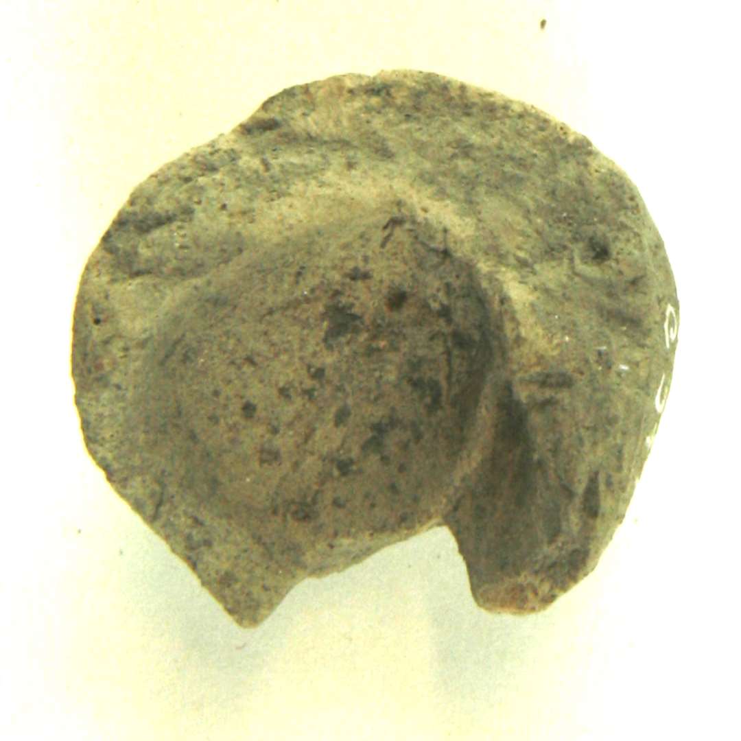 Fragment af en lille gråbrun lergenstand af lighed med en nøddeskalstor miniatureudgave af et halvkugleformet lerkar med indadbøjet mundingsrand. Omtrent halvdelen af genstanden er til stede. Højde: ca. 2,2 cm. Største tværmål: ca. 2,3 cm.