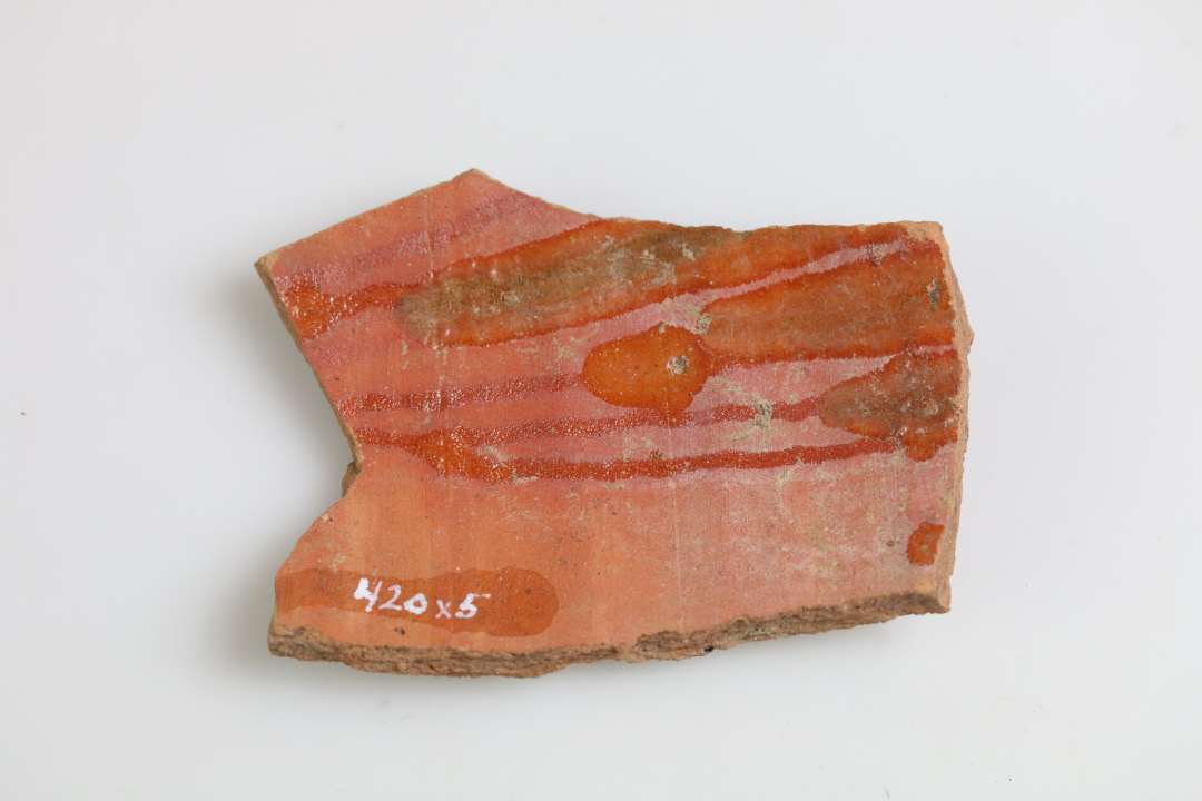 1 sideskår af kande, rødbrændt med pibeler og rullestempeldekor, hvorover klar blyglasur på ydersiden