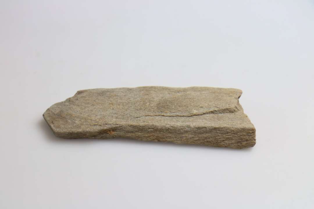 1 fragment af hvæssesten af gråligt, finkornet sandsten, uden synlige slidespor, afbrudt i begge ender, og smalnende til mod den ene, tilspidsende ende. Længde: 12,3 cm. Største bredde: 3,5 cm. Tykkelse: 1,3 cm.