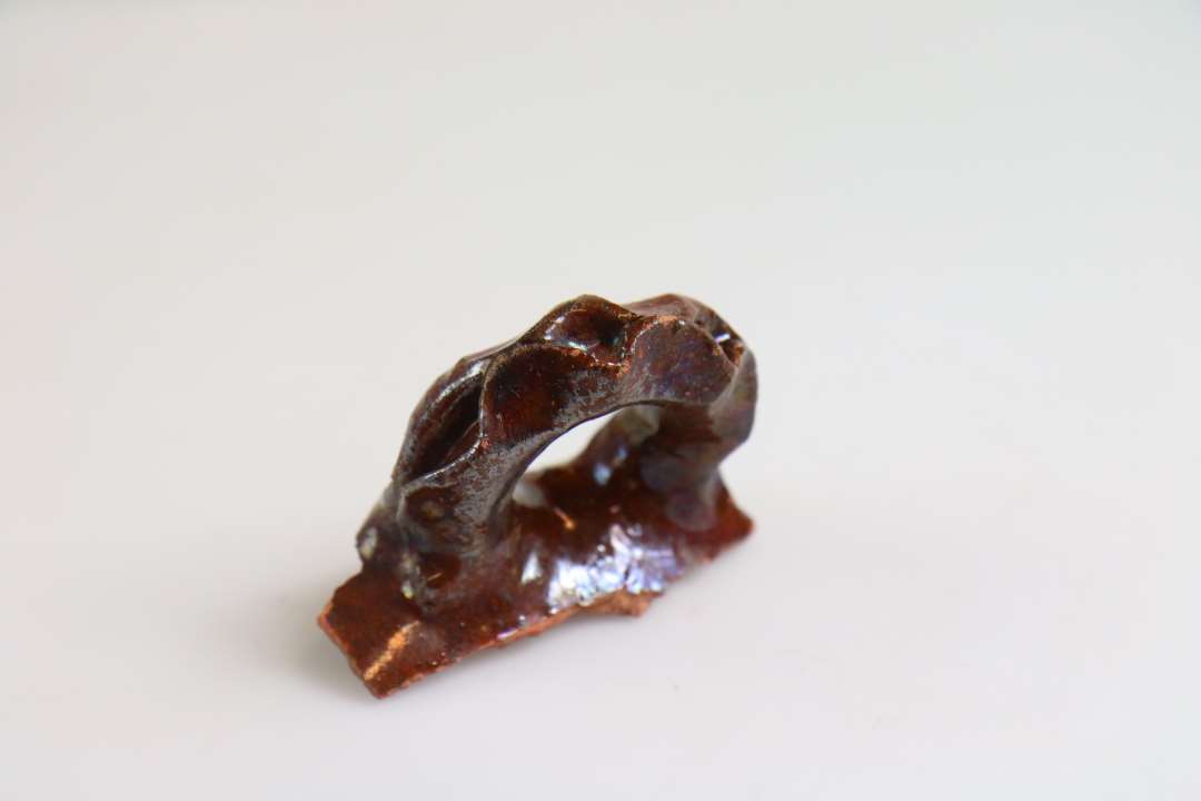 1 vandretsiddende øre fra øreskål af rødbrændt ler med klar blyglasur. Øret dekoreret med fingerindtryk