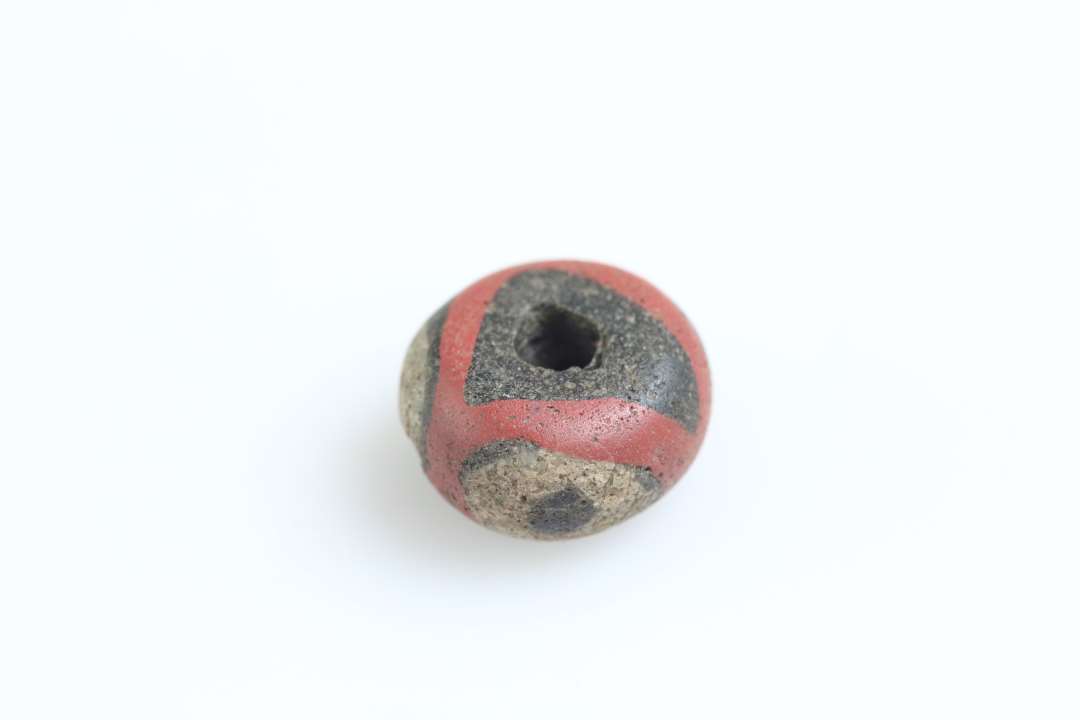 1 blåsort glasperle med røde og gullig/hvide indlægninger 'øjeperle'. diameter: 1 cm.