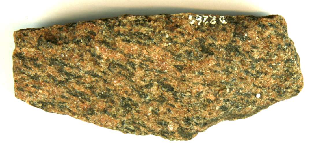 Afslag af en granitkvader. Rødlig med grå pletter. 2 behugne flader, som står i vinkel på hinanden. L : 16,5 cm.