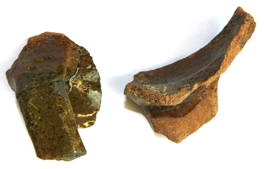 To hankebasisfragmenter af rødgodskander med flade bøjleformede hanke af trindt ovalt tværsnit, det ene med grønlig, det andet med klar blyglasur.