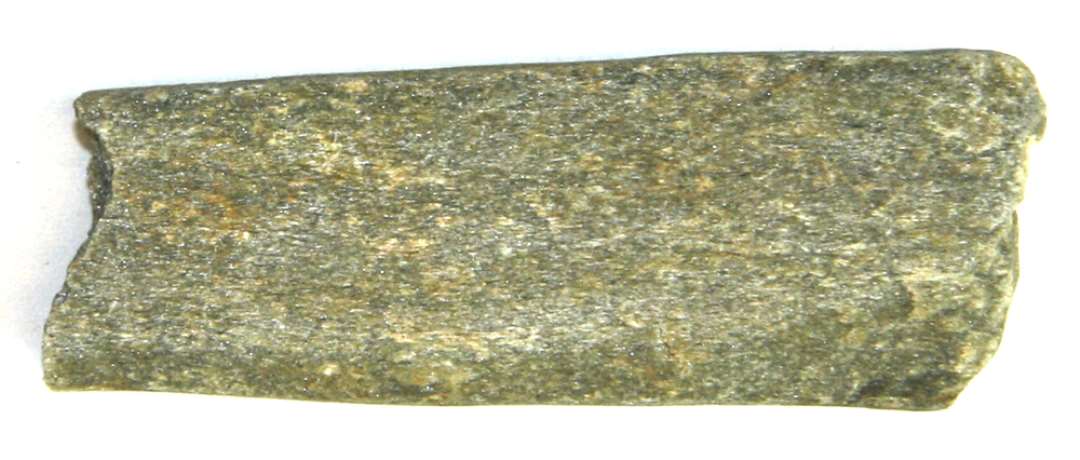 Fragment af flad stangformet hvæssesten af grålig sandsten, brudflader i begge ender, det ene hidrører fra fremgravningen. Længde: ca 6 cm, br.: ca 2,2 cm, tykkelse: ca 0,75 cm.