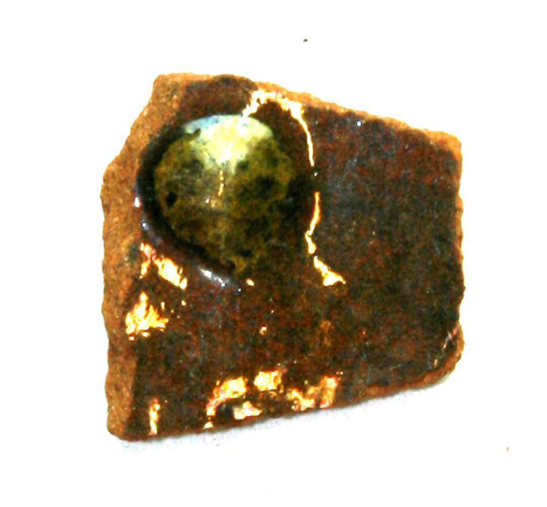 Bugskår af rødbrændt lergods, pålagt knop af pibelersmasse, i øvrigt klar til svagt grønlig blyglasur.