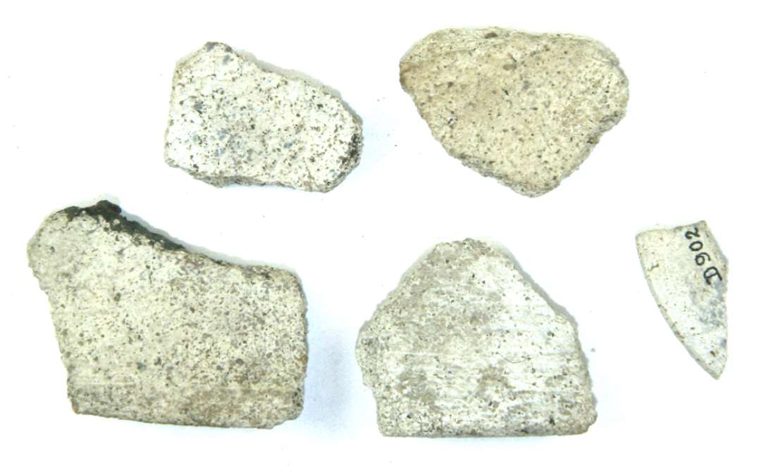 Fem fragmenter af hvidgrå, grynet stentøjsmasse, heraf tre randskår, de to med flad indadskrånende rand, det tredie med jævnt afrundet udadbøjet rand; desuden to bugskår.