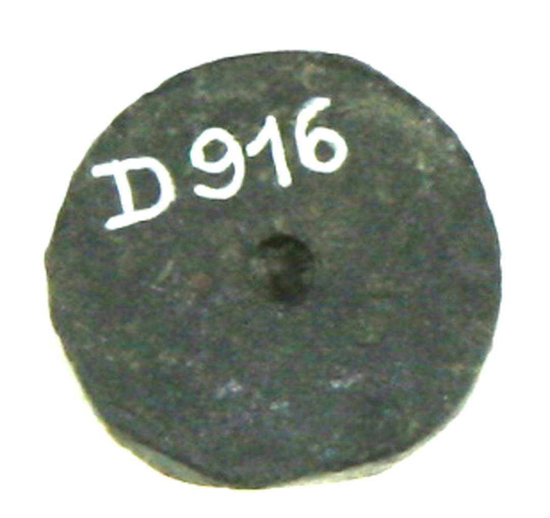 Vægtlod af bly af flad, uregelmæssig cirkelrund skiveform med facetter som efter tilskæring langs kanten. En cirkelformet grube findes i centrum af den ene fladside. Diam.: ca 1,3 cm., tykkelse: ca 0,6-0,65 cm. 