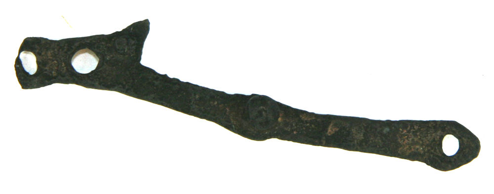 Kobberfragment bestående af en ca 7,7 cm lang, ca 0,5 - 0,6 cm bred og ca 0,2 cm tyk, forbøjet kobberstang med større bredde ved begge ender og på midten, hvor naglehuller findes. Ved stykkets ene ende, der tresidig afrundet, findes eet naglehul, ved den modsatte ende, hvor en tresidet udtungning er udhamret å den ene side, findes tre (det ene med stump af nagle), på stangens midte eet med isiddende nagle med massivt halvkugleformet hoved. Stykkets overflade er nu stærkt koparret og ornamentspor vanskelige at fastslå. Med forgyldning?

Fra vægt?