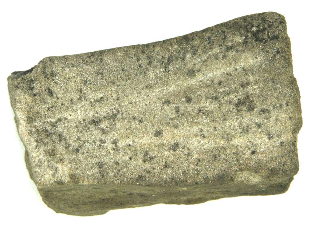 Fragment af hvæssesten af grålig sandsten. De tre af langsiderne bærer slibespor samt nedslebne furer. Længde ca 8,5 cm., tykkelse/bredde: ca 4,45 cm.