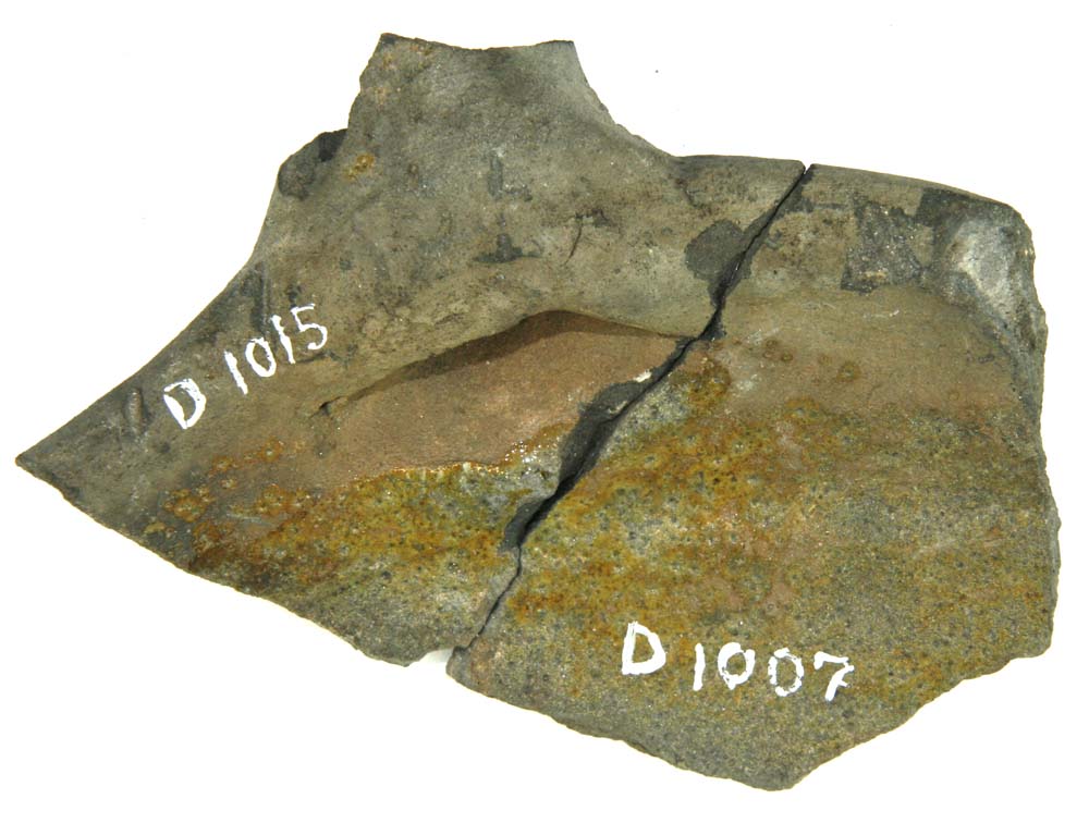 Randskår af stegefad, gråbrændt lergods med pletvis anbragt grønlig blyglasur på indersiden. På ydersiden findes en fladrygget bred vulst. Sammenlimet med D1015.