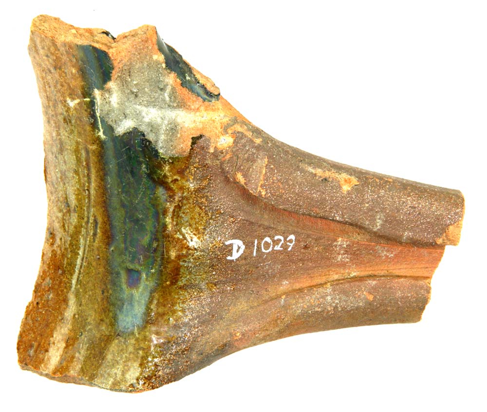 Fragmenteret håndtag fra stegefad med tilhørende mundingsrandsparti af rødbrændt lergods med klar til svagt grønlig blyglasur på indersiden. Skaftet har to furer på oversiden adskilt af en skarprygget kam, ligesom begge sider på skaftets overkant er delvis bøjet ind over furerne. 