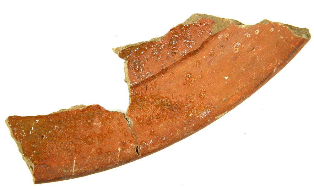 Randskår af stegefad eller skål af rødbrændt lergods med grå skærv, pletvis klar blyglasur på indersiden.