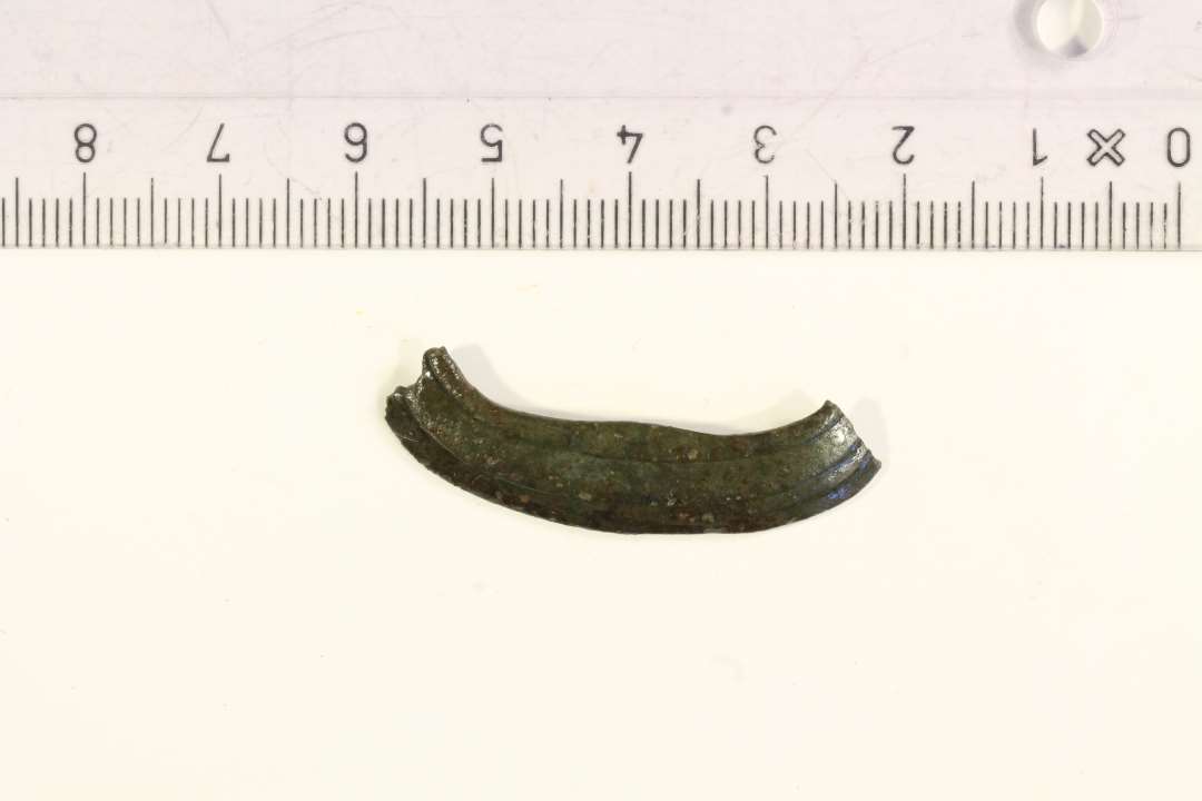 1 fragment af større remspænde af bronze. største mål: ca 3,5 cm.