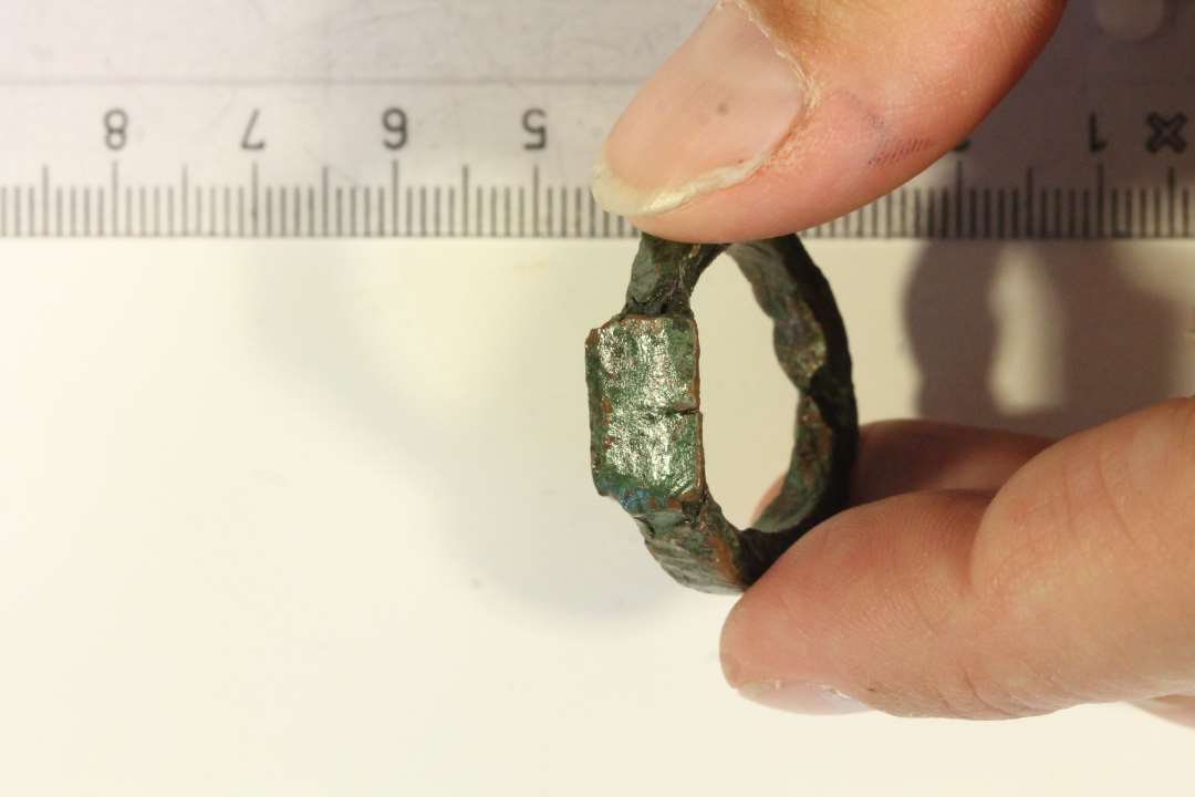 1 noget groft tildannet  'plumb'  fingerring af bronze, med rektangulær plade. Kraftig skinne. Ydre diameter: 2,8 cm., indre diameter: ca 1,9 cm.