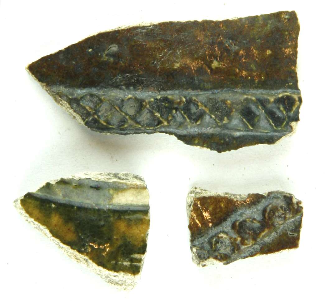 Tre skår fra kander af hårdtbrændt pibelersmasse med spættet klar og sortbrun blyglasur, de 2 med pålagte bånd med indpressede rhombeformede ornamenter.