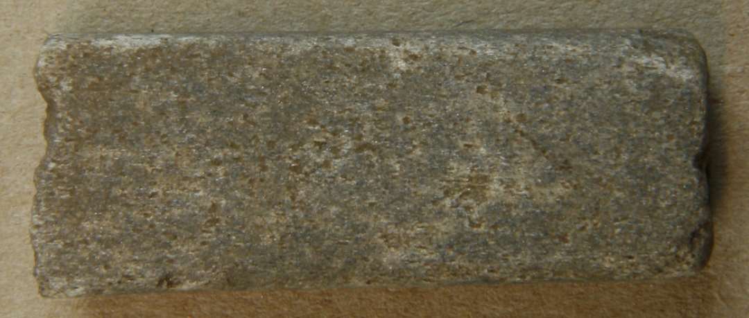 Fragment af aflang, firsidet hvæssesten. Mål: 45x17 mm.