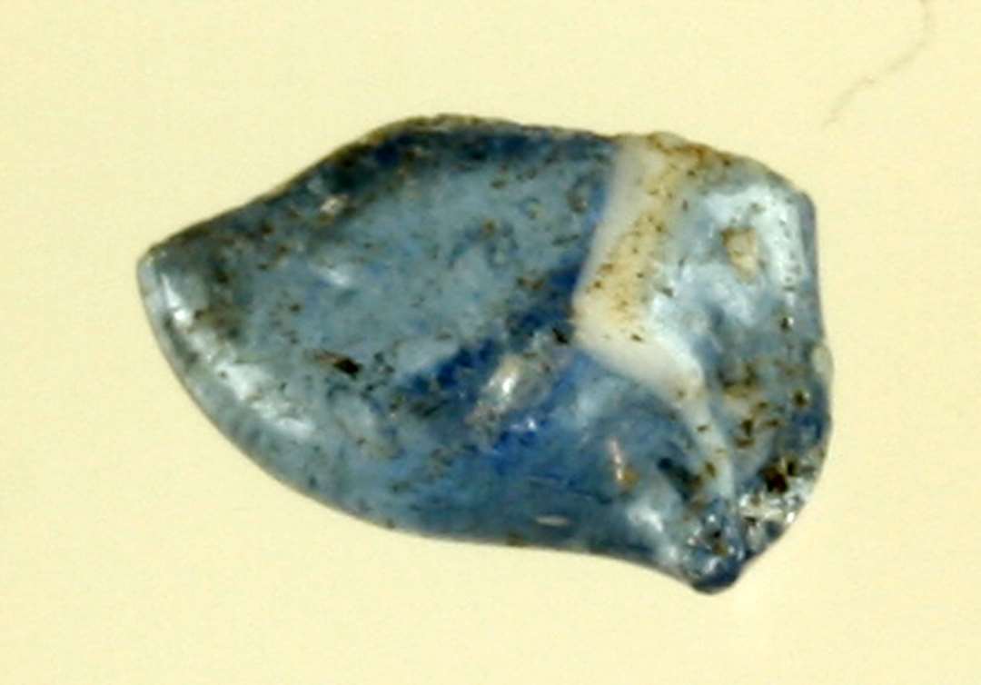 1 ubetydelig stump af smeltet, delvis fladklemt dråbe af gennemsigtigt blåligt glas, hvori en enkelt tråd af hvidlig uigennemsigtig glasmasse.
