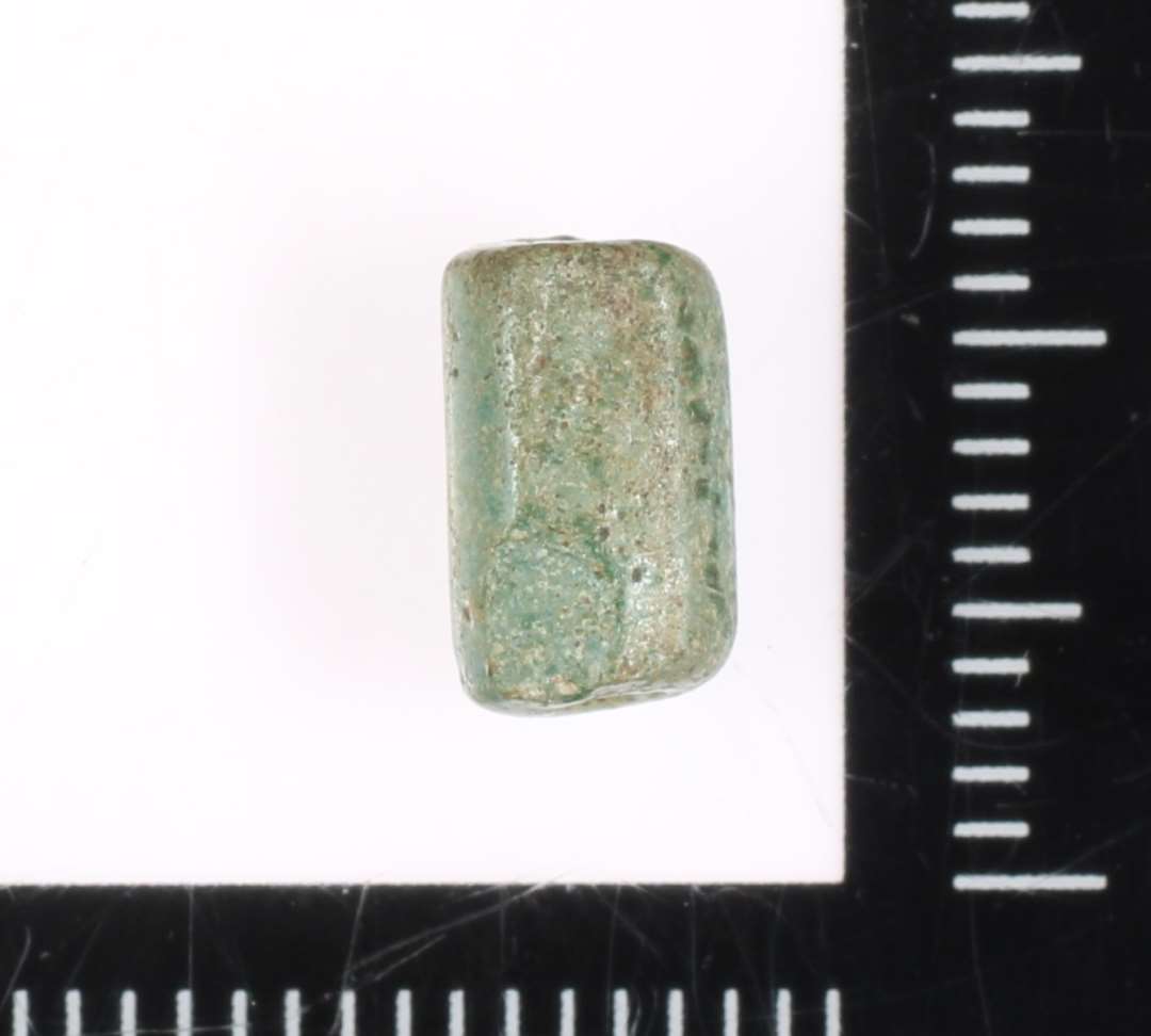 En lille sammensmeltet cylinderformet perle af svag grønlig glasmasse. 9 mm.