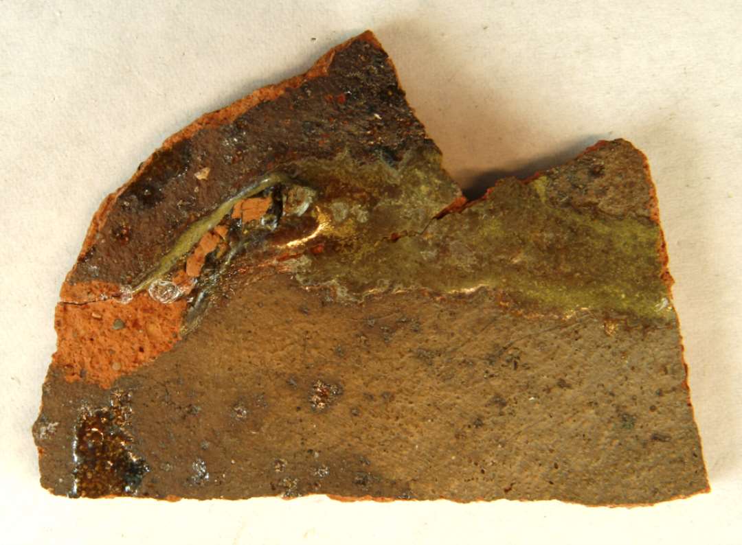 1 bundskår af rødbrændt lergods med ujævn, klar til grønlig blyglasur på ydersiden. Gruppe 1. Flamsk