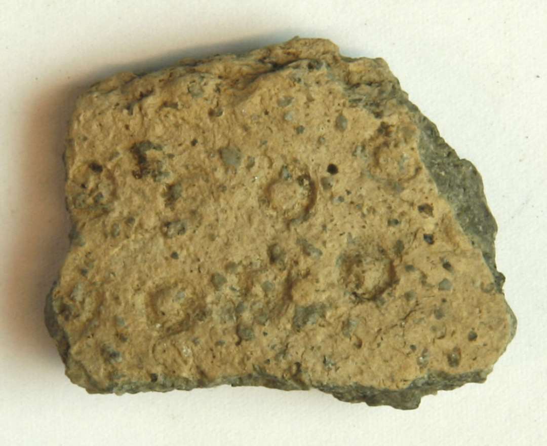 1 skulderskår af gulliggråt, magret lergods med indstemplede cirkelformede ornamenter.