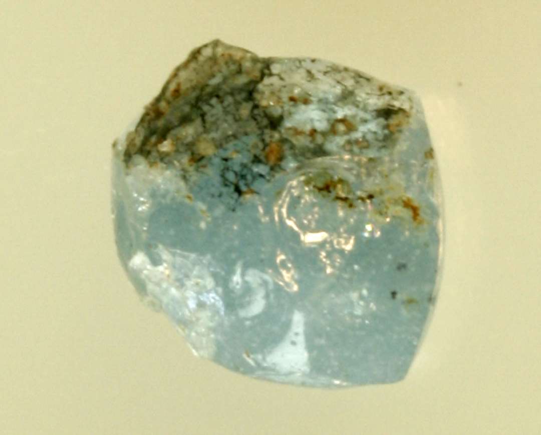 1 klump gråblåt glas, overfladen dels med indsmeltede urenheder, dels afslåede brudflader. St. L: 0,9 cm.