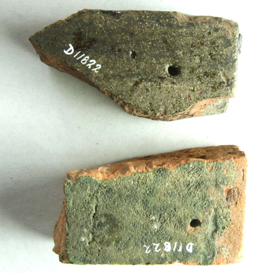 2 hjørnefragmenter af gulvfliser af rødbrun ler. Den ene med brun glasur på overside og kanter, den anden med grøn glasur på overside. Tyk: 2,5 (brune) og 2,8 cm.