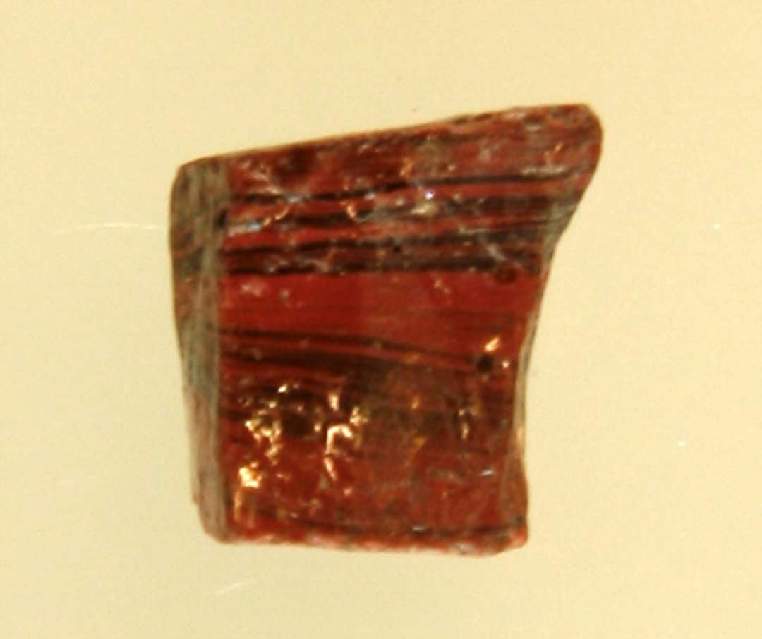 1 fragmenteret (?) mosaikstift af rødbrunlig, sortstribet ugennemsigtig glasmasse.