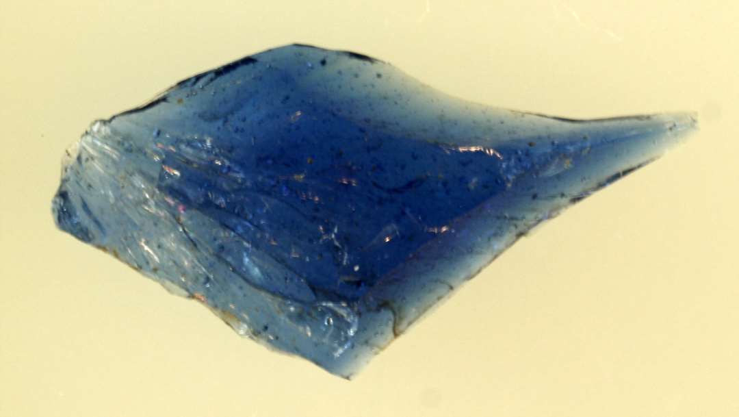 1 stykke råglas af flad rhombeagtig form med lang spids i den ene ende af blåligt gennemsigtigt glas.