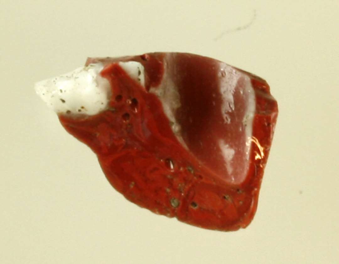 1 fragment af smeltet klump glas af rødbrunlig ugennemsigtig masse, med rester af indsmeltet hvidlig ugennemsigtig glasmasse.