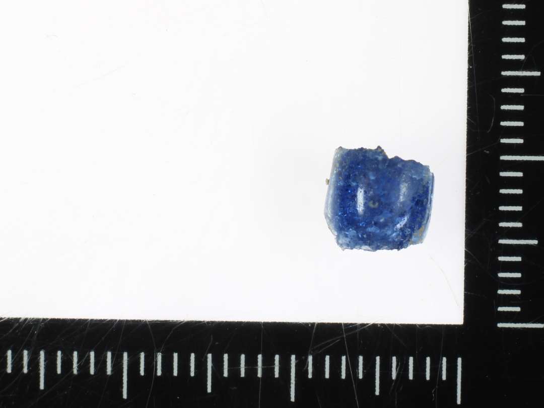 1 fragment af perle af fladtrykt kugleform af blåligt gennemsigtigt glas. 5 mm.