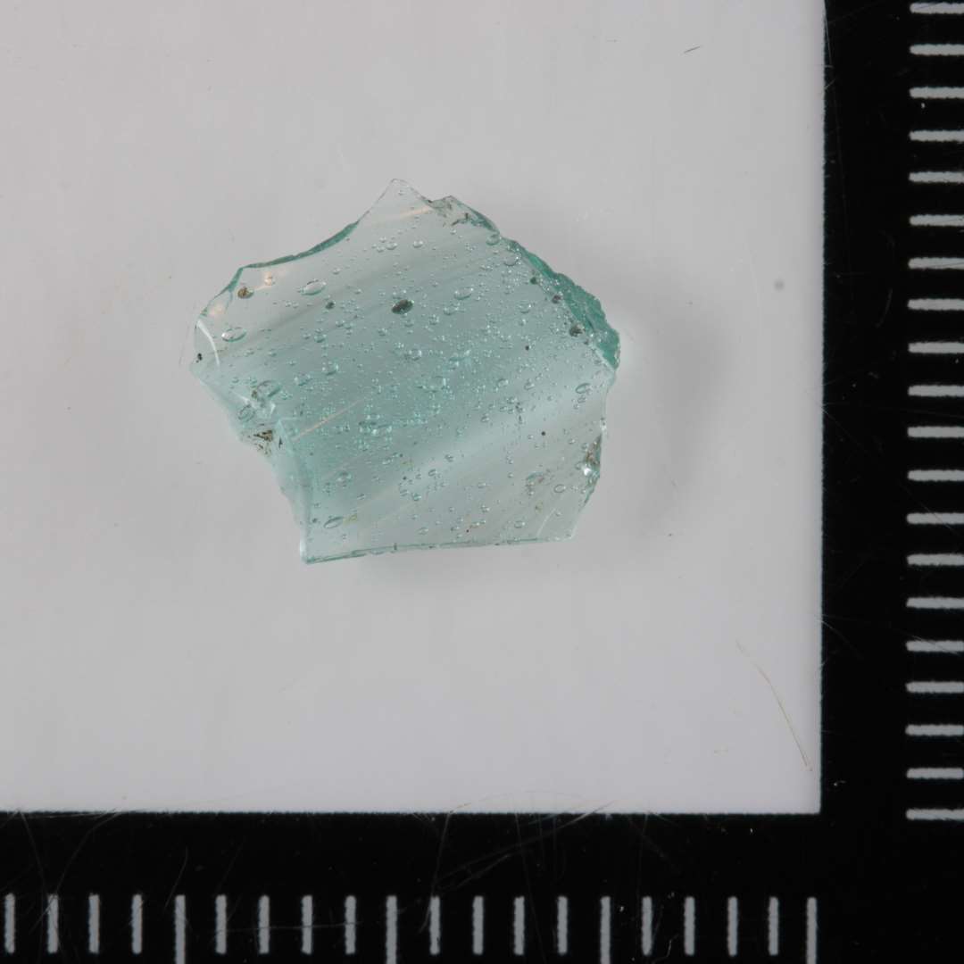 1 ubetydeligt sideskår af svagt grønligt, gennemsigtigt glas med flad vulstformig fortykkelse på midten.