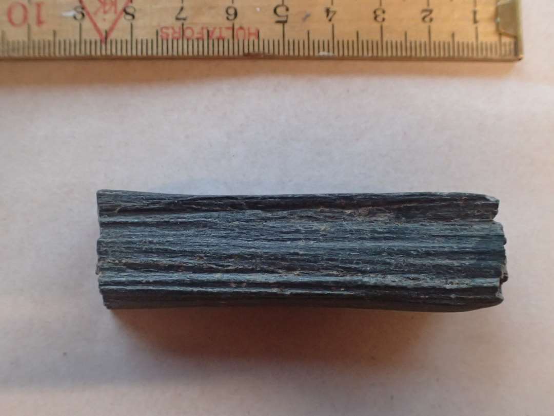 1 fragment af stangformet hvæssesten af grålig skifer overbrudt på midten L: 7,8 cm.