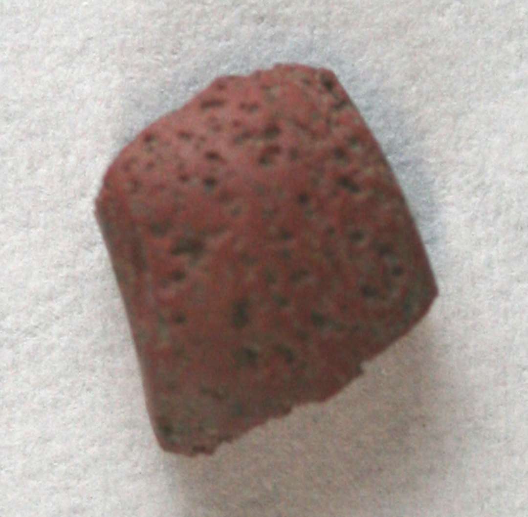 1 fragment af cylinderformet perle med svagt hvælvet yderside af rødbrunlig ugennemsigtig glasmasse. 10 mm.