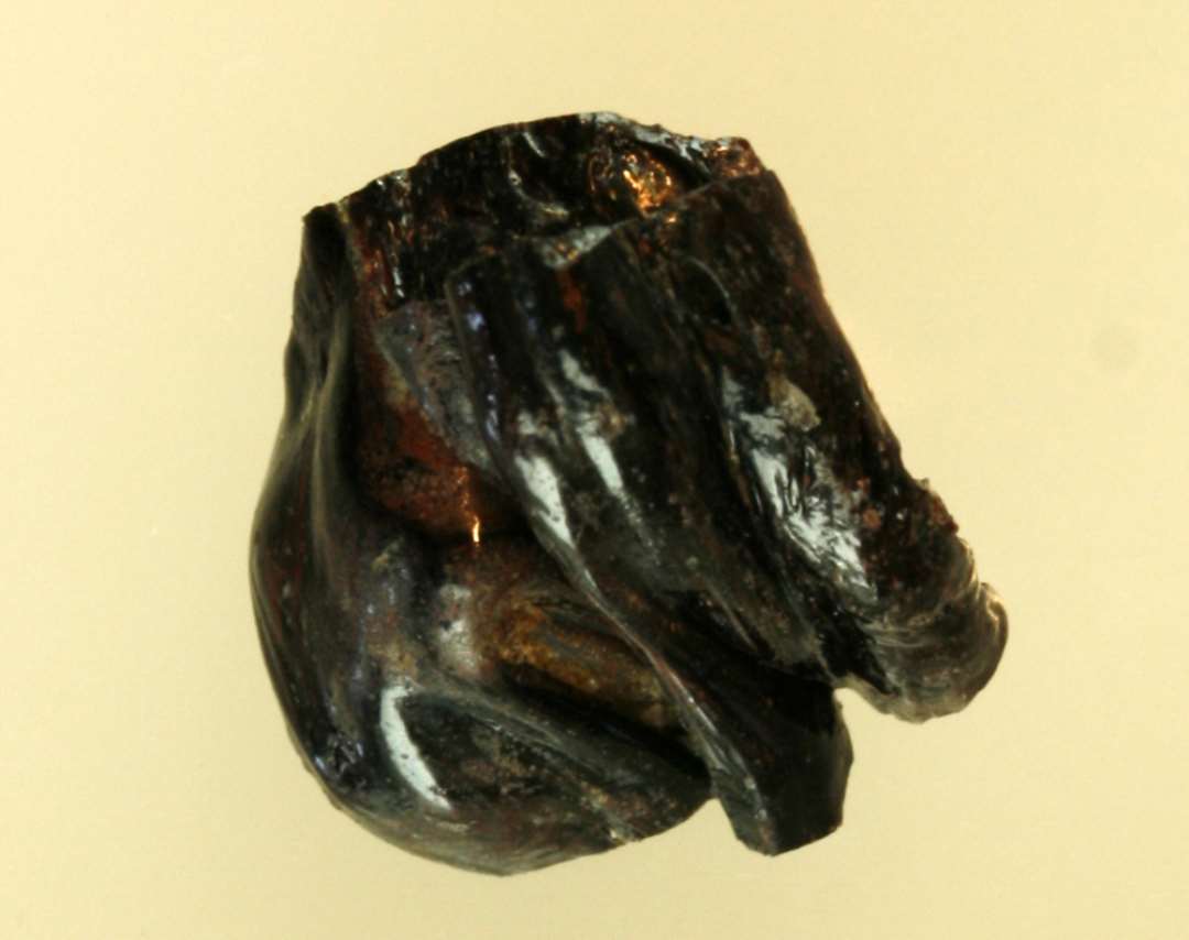 1 fragment af smeltet glasklump af sortbrun, ugennemsigtig glasmasse hvori årer af rødbrunt ugennemsigtigt glas.