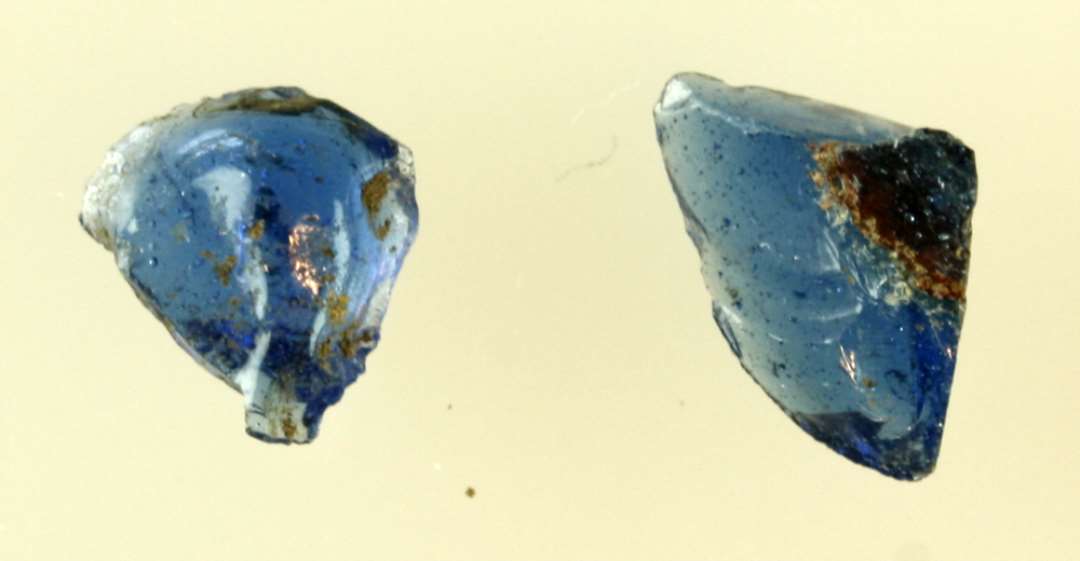 2 stykker råglas af blåligt gennemsigtigt glas. I det ene stykke findes en stribe af rødbrunlig ugennemsigtig glasmasse.