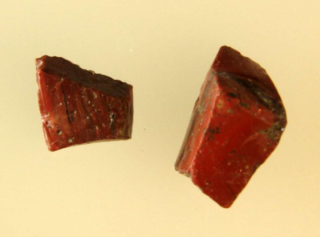 2 råglasstykker af rødbrunlig ugennemsigtig glasmasse, hvori årer af gennemsigtigt glas, der fremtræder som mørke striber.