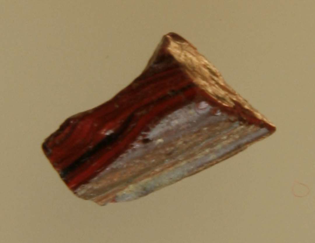 Fragment af mosaikstift af rødbrunlig ugennemsigtig glasmasse hvori tynde mørkt fremtrædende striber.