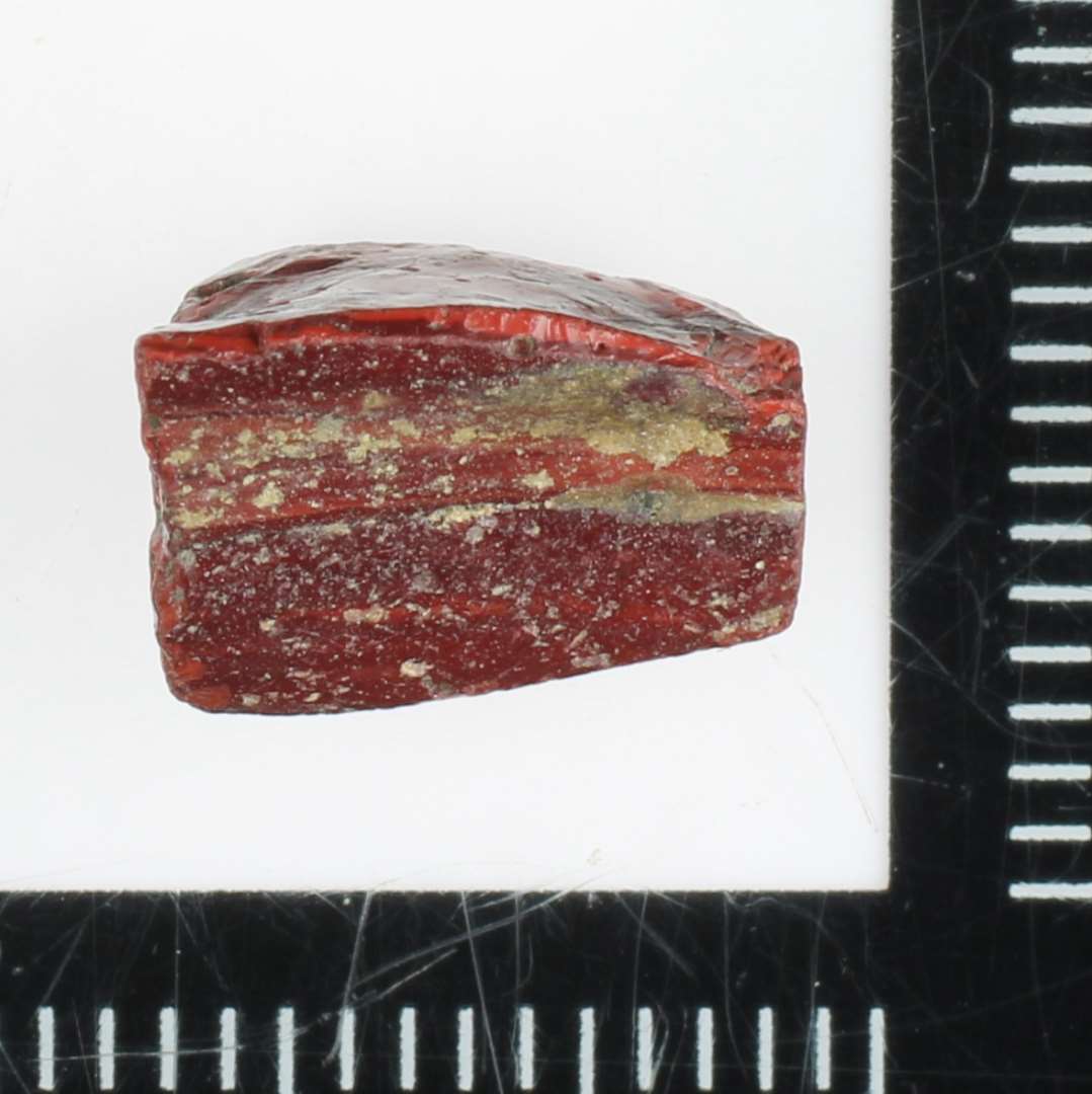Fragment af mosaikstift af rødbrunlig ugennemsigtig glasmasse hvori tynde mørkt fremtrædende striber.