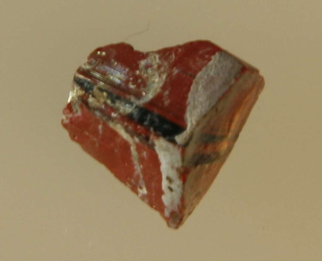 Fragment af mosaikstift af rødbrun glas med blå årer. St. L: 1 cm.