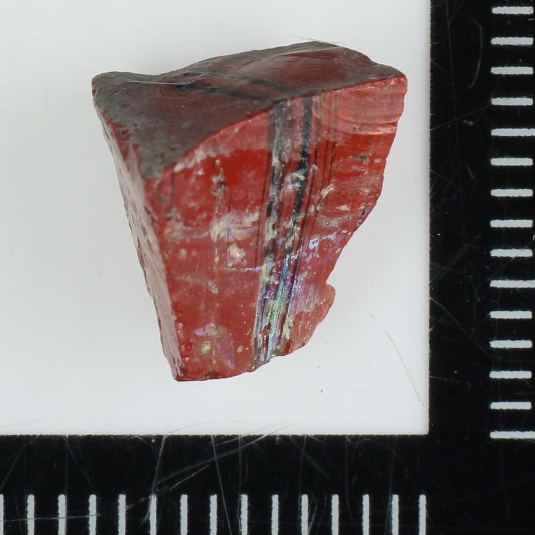 Fragment af mosaikstift af rødbrun glas med blå årer. St. L: 1 cm.