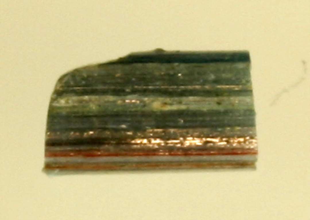 1 fragment af stav af blåt glas med indlagte røde og hvide tråde. L: 0,7 cm.