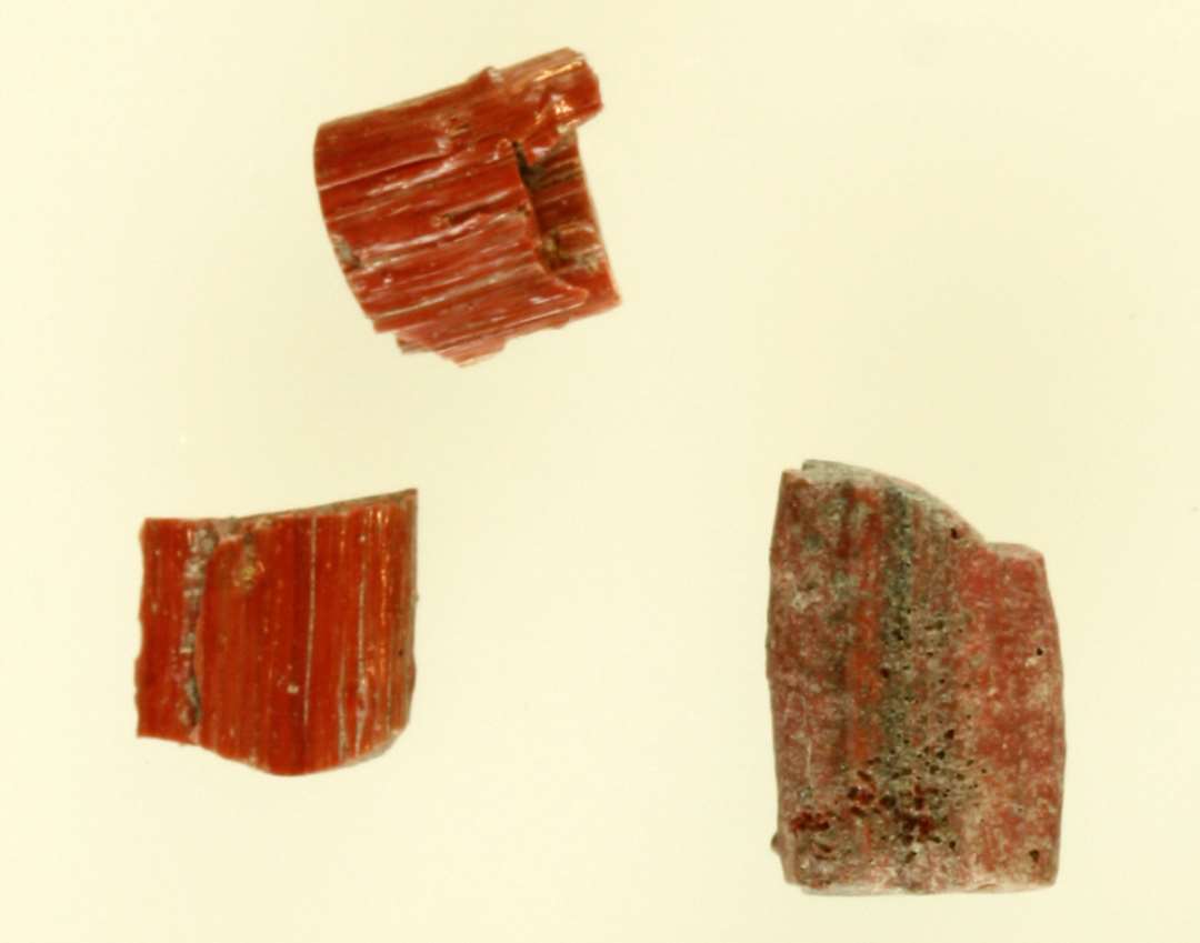 3 fragmenter af stave af rødbrunt glas med indlagte blå tråde.
